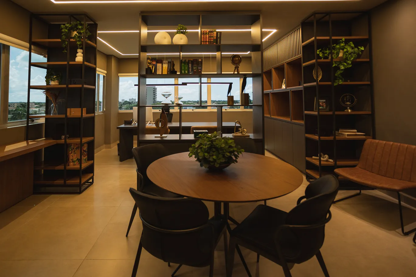 Escritório de advocacia sofisticado com mesa redonda de madeira nobre, cadeiras estofadas em couro, estantes repletas de livros jurídicos iluminadas indiretamente e vista panorâmica da cidade ao fundo, paleta de tons marrom, dourado e cinza escuro, iluminação quente e cinematográfica de fim de tarde, ângulo amplo, fotografia profissional ultra-realista